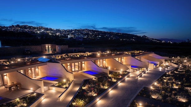Un resort moderno con varias piscinas, un jardín ajardinado y una vista a un pueblo lejano al atardecer.
