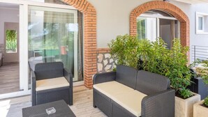 A patio area with wicker furniture, a glass door leading to a balcony, and potted plants. - Charming 4-bedroom estate in enchanting Albaré Stazione with AC, WiFi (Albaré Stazione)