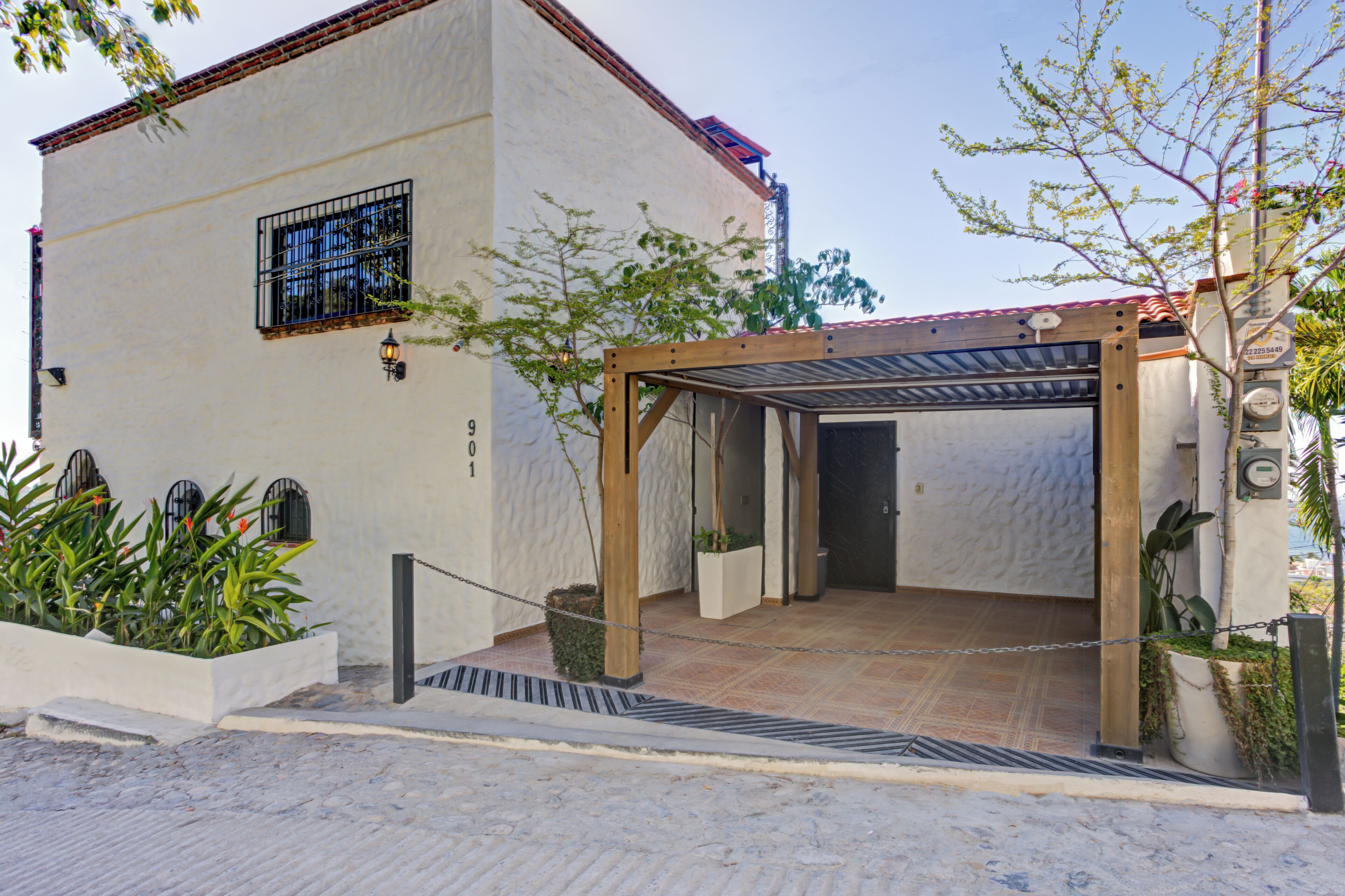 A building with a white exterior, a wooden pergola, and a chain-link fence.