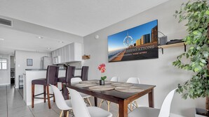 A modern dining area with a wooden table, white and brown chairs, and a cityscape painting on the wall. - Perfect beach getaway at Fountainhead Towers, located oceanfront on 116th Street (Ocean City)