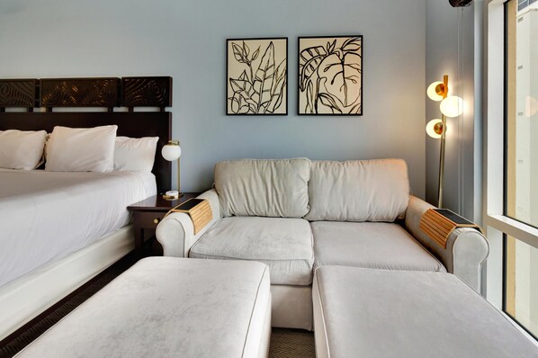 A hotel room with a bed, a sofa, and two artwork pieces on the wall.