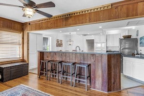A kitchen with wooden accents, a central island with stools, and a ceiling fan.