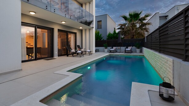 A modern outdoor pool area with a glass balustrade, lounge chairs, and a well-maintained garden. - Villa Sanja Zadarvillas (Nin)