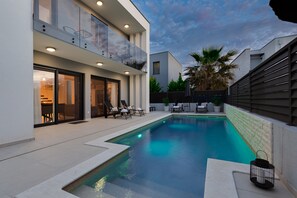 A modern outdoor pool area with a glass balustrade, lounge chairs, and a well-maintained garden. - Villa Sanja Zadarvillas (Nin)