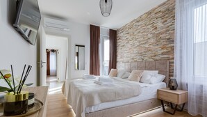 A modern bedroom with a large bed, a wooden nightstand, a TV mounted on the wall, and a brick accent wall. - Villa Sanja Zadarvillas (Nin)