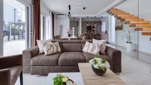 A modern living room with a brown sectional sofa, a coffee table, and a staircase with wooden steps. - Villa Sanja Zadarvillas (Nin)