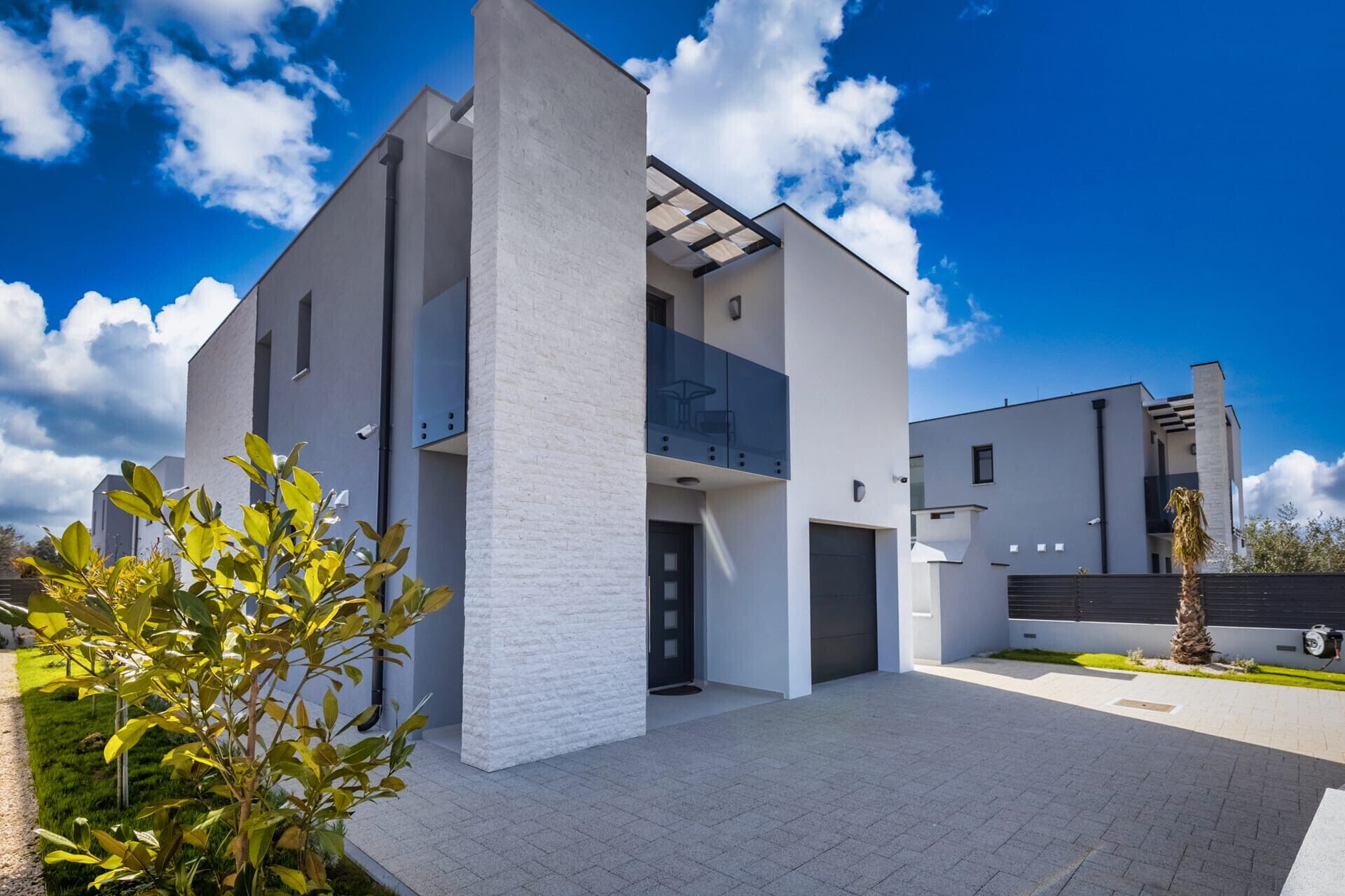 A modern two-story house with a flat roof, large windows, and a balcony.