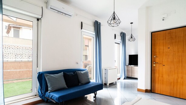 A modern living room with a blue sofa, a TV, and a wooden door. - Lovely Terrace Apartment by Wonderful Italy (Bari)
