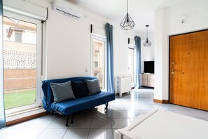 A modern living room with a blue sofa, a wooden door, and a view of a garden.