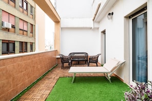 A small outdoor patio with a table and chairs, a bench, and a small patch of artificial grass.