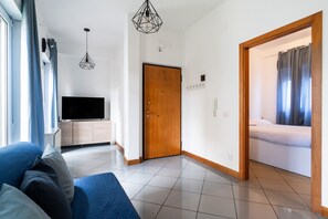 A modern hotel room with a flat-screen TV, a wooden door, and a bed with a white duvet.