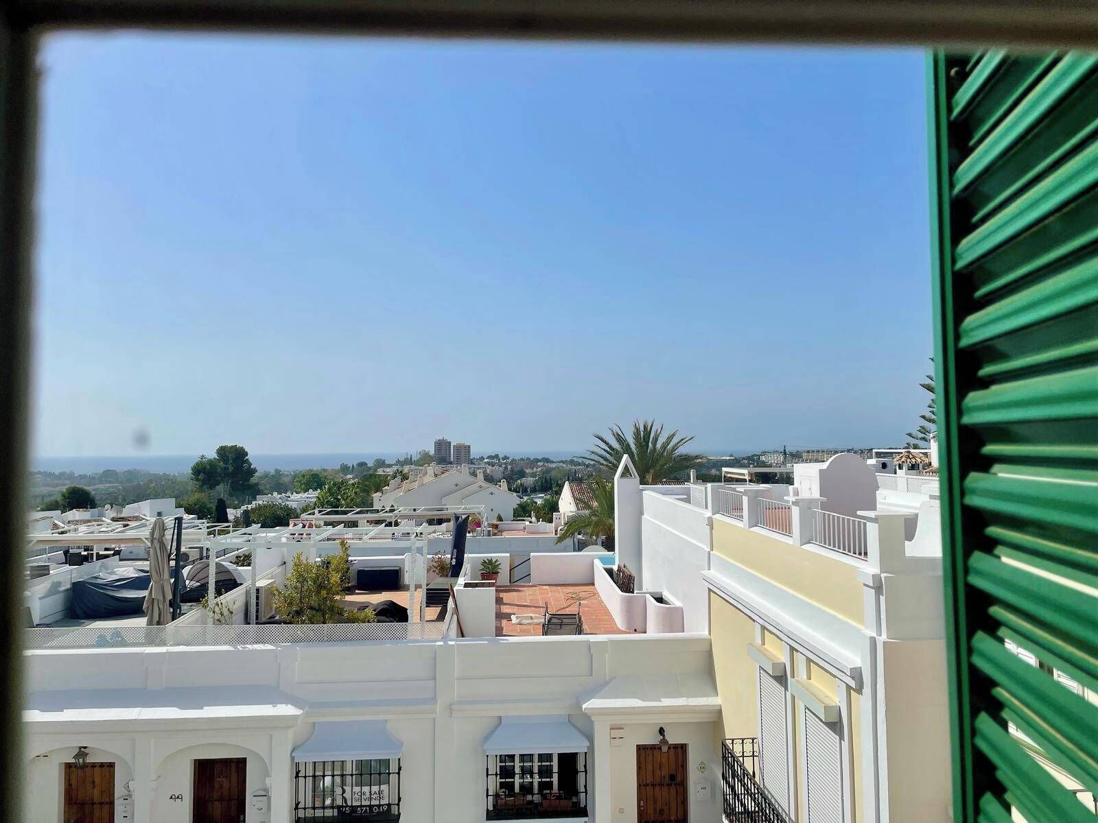 Μια οικιστική περιοχή με λευκά κτίρια, θέα στη θάλασσα και ένα φοινικόδεντρο.
