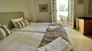 Una camera d'albergo con due letti, un tavolino, una sedia e un balcone con vista.