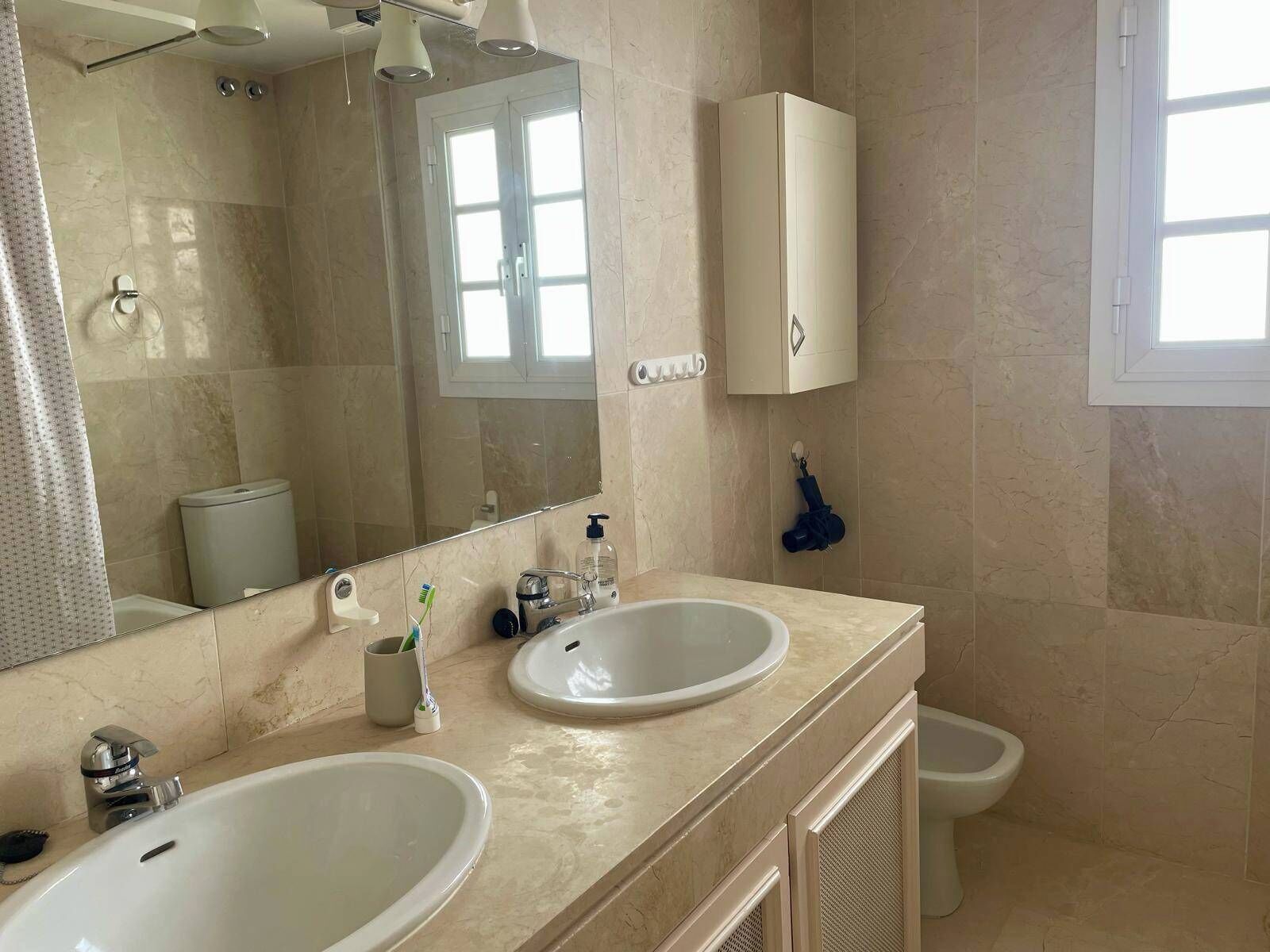 Une salle de bain avec deux lavabos, des toilettes, un miroir et une fenêtre.