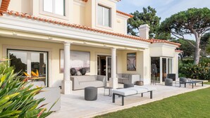 A modern house with a patio area featuring outdoor furniture, a well-maintained lawn, and a large tree. - Fairview Villa by Cadenzalux (Cascais)