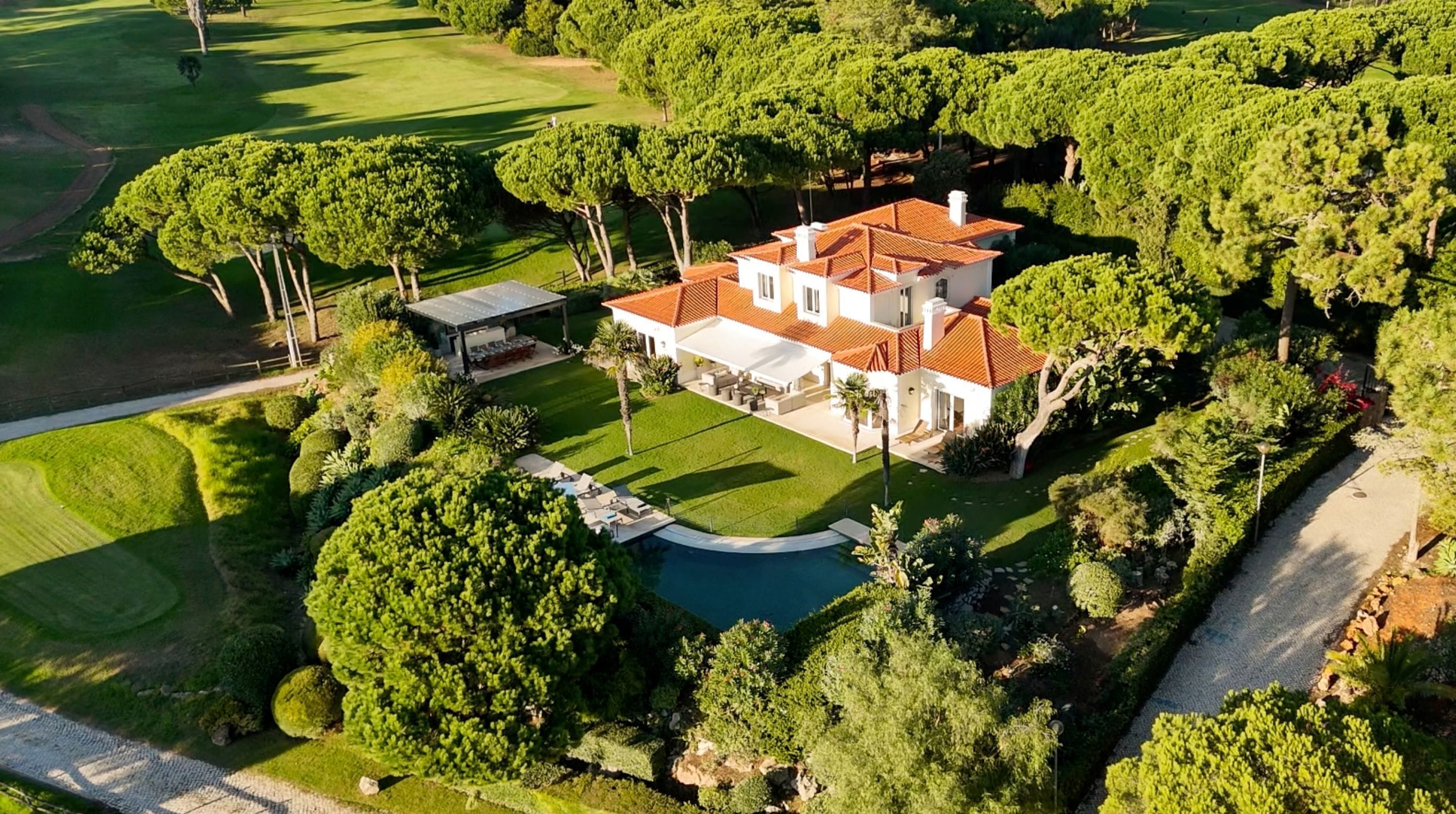 A large, two-story house with a swimming pool, surrounded by well-maintained gardens and trees.