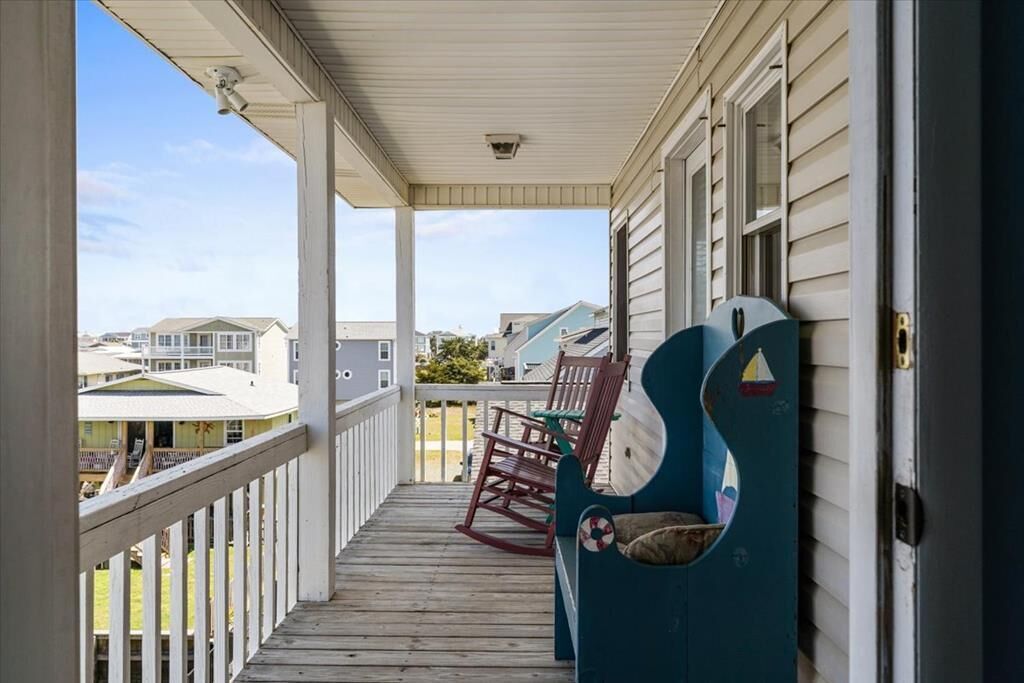 Une véranda couverte avec une balustrade en bois, une chaise berçante bleue et un banc orné d'un motif représentant un gilet de sauvetage.