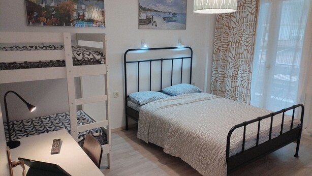 A bedroom with a bunk bed, a desk with a lamp, and a bed with patterned bedding.
