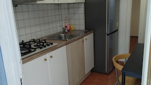 A compact kitchen with white cabinets, a gas stove, a stainless steel sink, and a refrigerator.