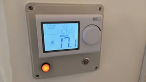 A thermostat with a digital display indicating room temperature at 17.1°C, a system heat setting at 26.5°C, and an EMOS label.