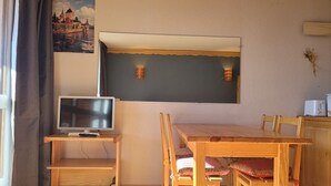 Une pièce comprenant une table et des chaises en bois, un téléviseur posé sur un meuble, et un tableau représentant un château accroché au mur.