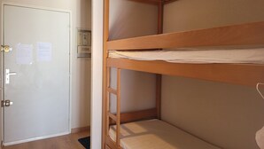 Une chambre avec un lit superpos é, une porte, un luminaire et un tableau électrique.