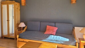 Un meuble en bois avec des portes en verre, un canapé gris avec un coussin rouge et deux lampes fixées au mur.