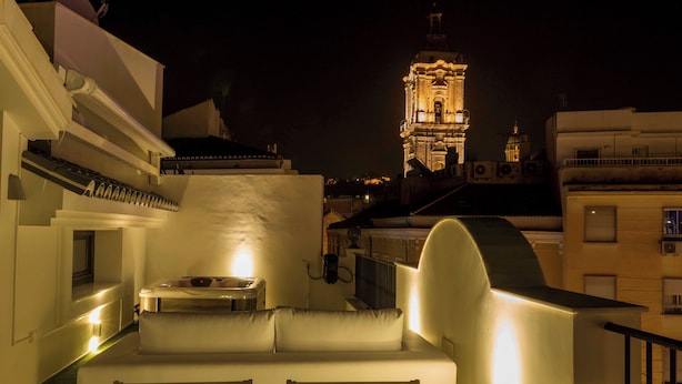 Une terrasse sur le toit, avec un canapé blanc et une table, d’où l’on peut admirer un paysage urbain, une tour illuminée se dressant à l’arrière-plan.