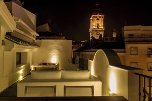 A rooftop terrace with a white sofa and a table, overlooking a cityscape with a lit-up tower in the background. - The Clock House Malaga  (Malaga)