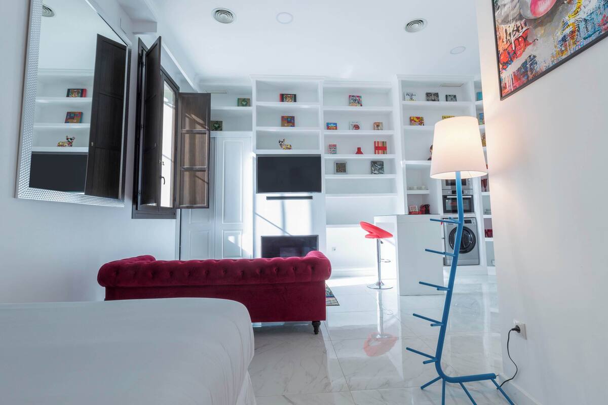 A modern bedroom with a red sofa, a large mirror, a TV, and a white wardrobe.