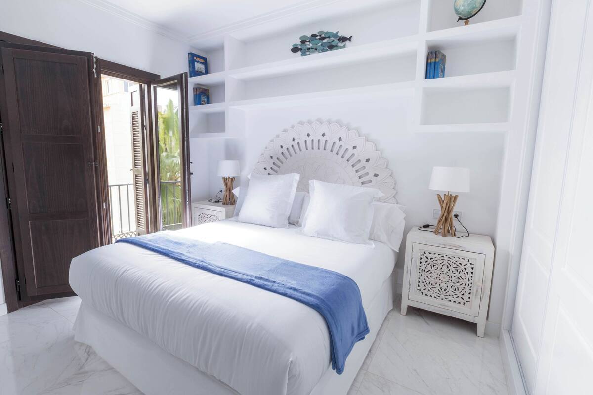 A bedroom with a large bed, white walls, and a wooden door.
