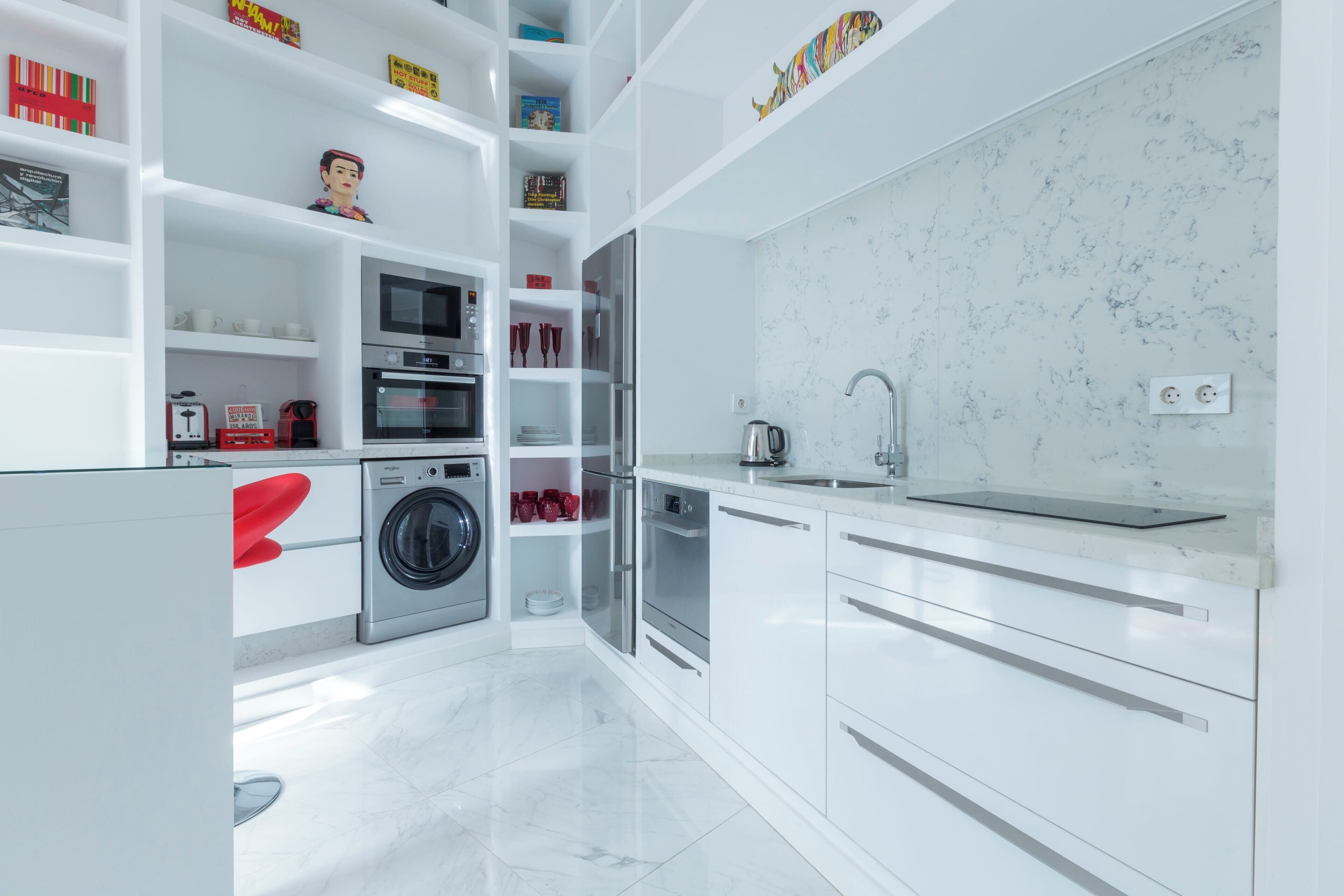 A modern kitchen with white cabinetry, a built-in oven, a washing machine, and a sink.