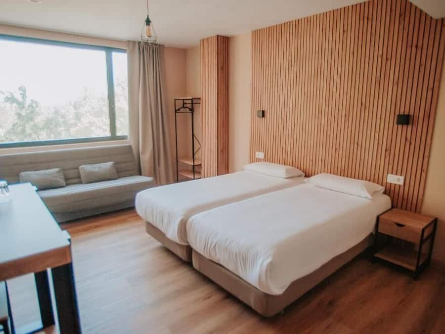 A modern bedroom with a large window, a wooden slatted wall, a sofa, and a desk.
