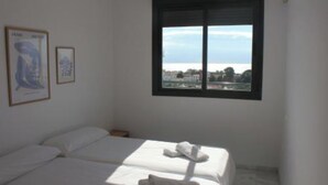 A hotel room with two beds, a large window with a view of a cityscape, and two framed pictures on the wall. - MANGATA APARTMENT IN NERJA (Nerja)
