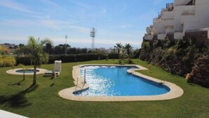 A swimming pool surrounded by a well-maintained lawn, with a multi-story building in the background. - MANGATA APARTMENT IN NERJA (Nerja)