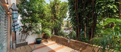 Relax in a tranquil outdoor space with a round table and two chairs, surrounded by lush greenery and a low wall overlooking the surrounding area.