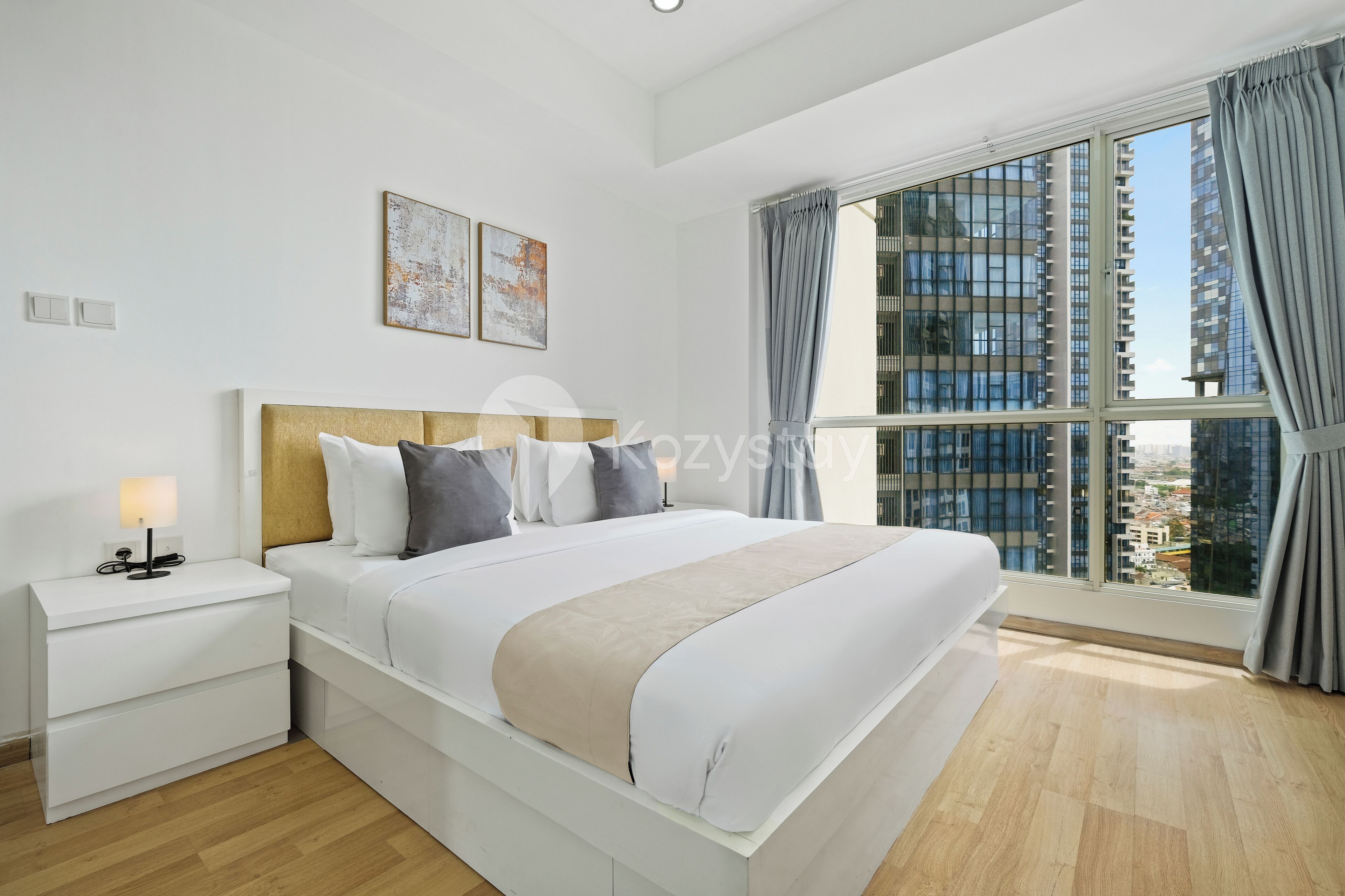 Camera moderna con un letto grande, comodini e vista su alti edifici attraverso un'ampia finestra.