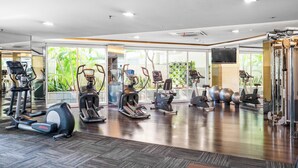 Ein Fitnessraum mit unterschiedlichen Trainingsgeräten, großen Fenstern und einem glatten Holzboden.