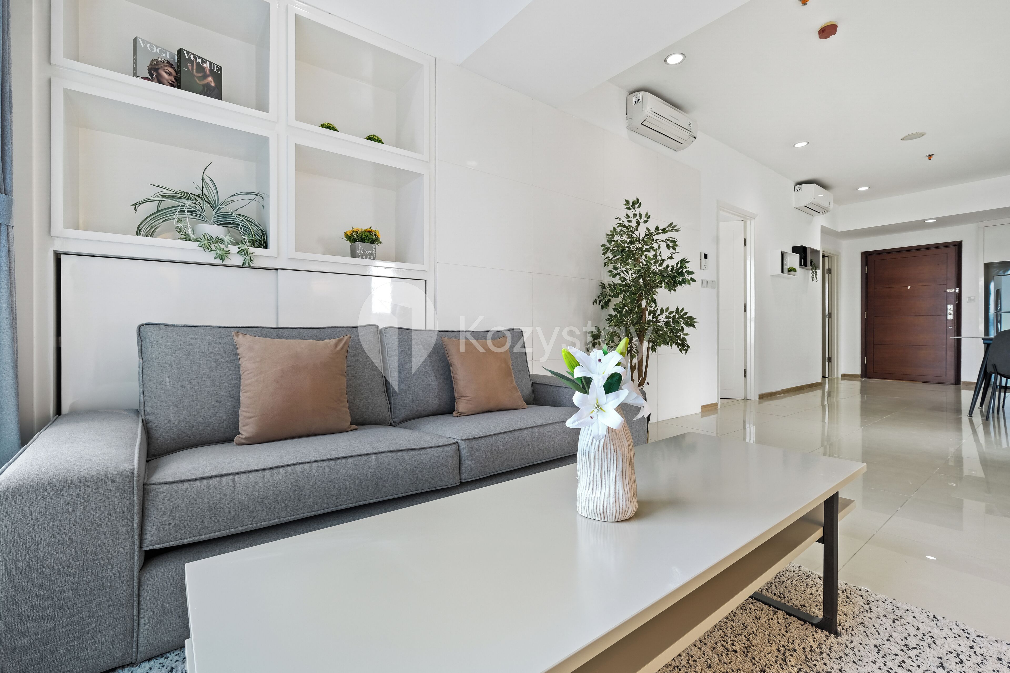 A modern living room with a grey sofa, white shelves, and a large plant.