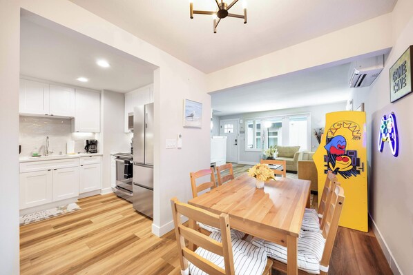 A modern kitchen with white cabinets, a wooden dining table, and a yellow decorative board.