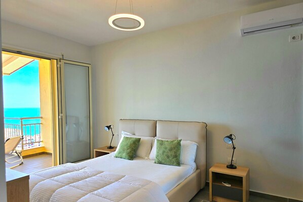 Habitación de hotel con cama, dos mesitas de noche, aire acondicionado en la pared y balcón con vistas al mar.