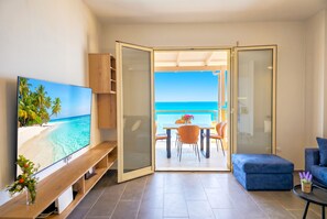 A modern living room with a TV, a blue sofa, and a dining area with a view of the ocean. - Hill Apartment with Sea View in Durres 061 (Durres)