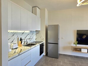 Uma cozinha moderna com armários brancos, bancada de mármore, forno embutido e geladeira de aço inoxidável.