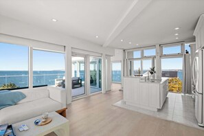 A modern interior with a balcony, a kitchen area, and a seating area with a view of the sea.