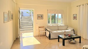 Un salon comprenant un canapé, une table basse en verre, un fauteuil, une fenêtre donnant sur un beau paysage et un escalier menant à l’extérieur.
