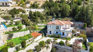 Une maison à deux étages, avec un toit recouvert de tuiles rouges, entourée de murs en pierre et de verdure.