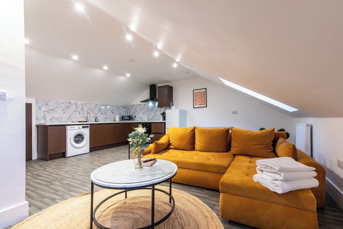A modern living room with a sofa, a coffee table, and a washing machine in the background.