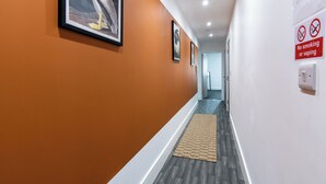 Un couloir aux murs orange, orné de tableaux encadrés, avec un panneau «interdiction de fumer» et un plancher en bois.