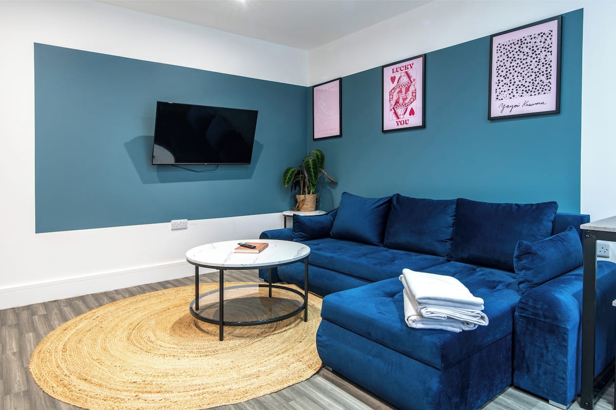 A modern living room with a blue sofa, a round coffee table, a flat-screen TV mounted on the wall, and framed artwork.