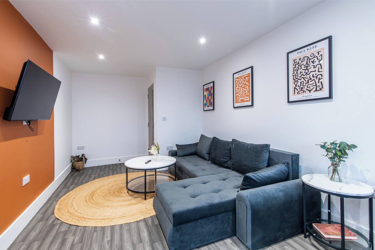 A modern living room with a sectional sofa, a round coffee table, and a flat-screen TV mounted on the wall.